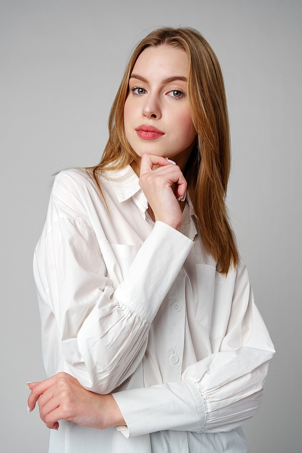 Young woman in white shirt, thoughtful pose.